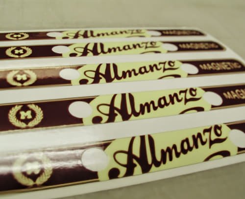 Custom 'Almanzo' stickers with maroon and gold designs lined up on a sheet for application.